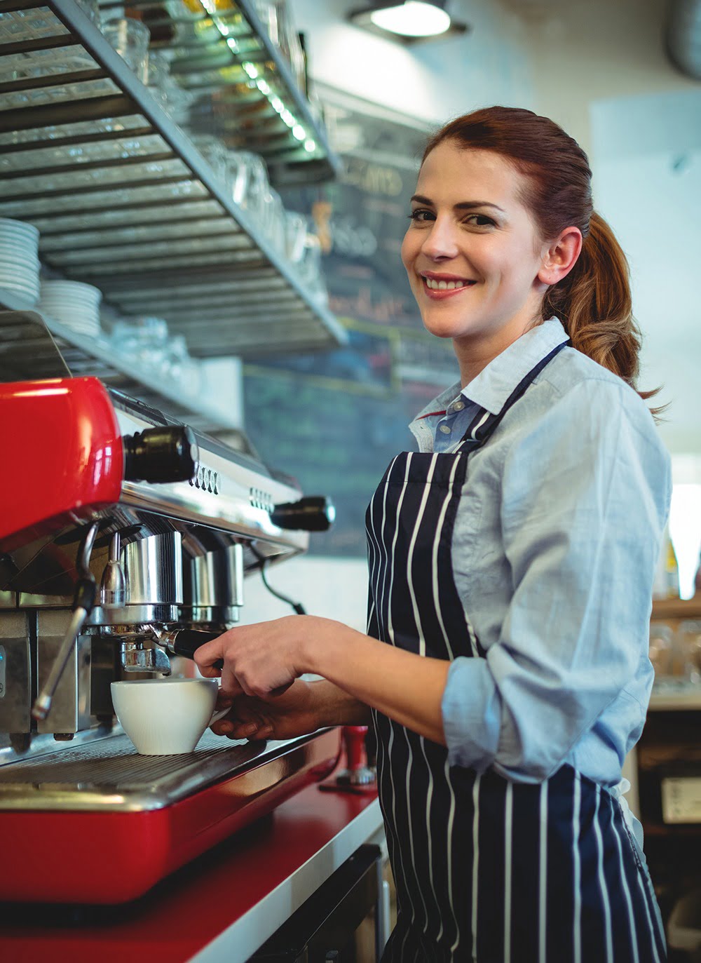 Portrait of happy waitress pouring coffee from espresso maker at cafe